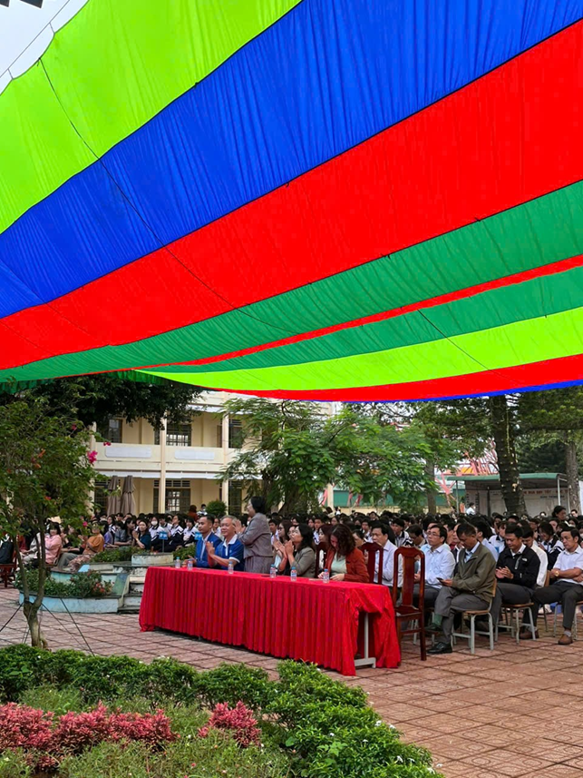 A group of people sitting on chairs under a large striped fabricDescription automatically generated